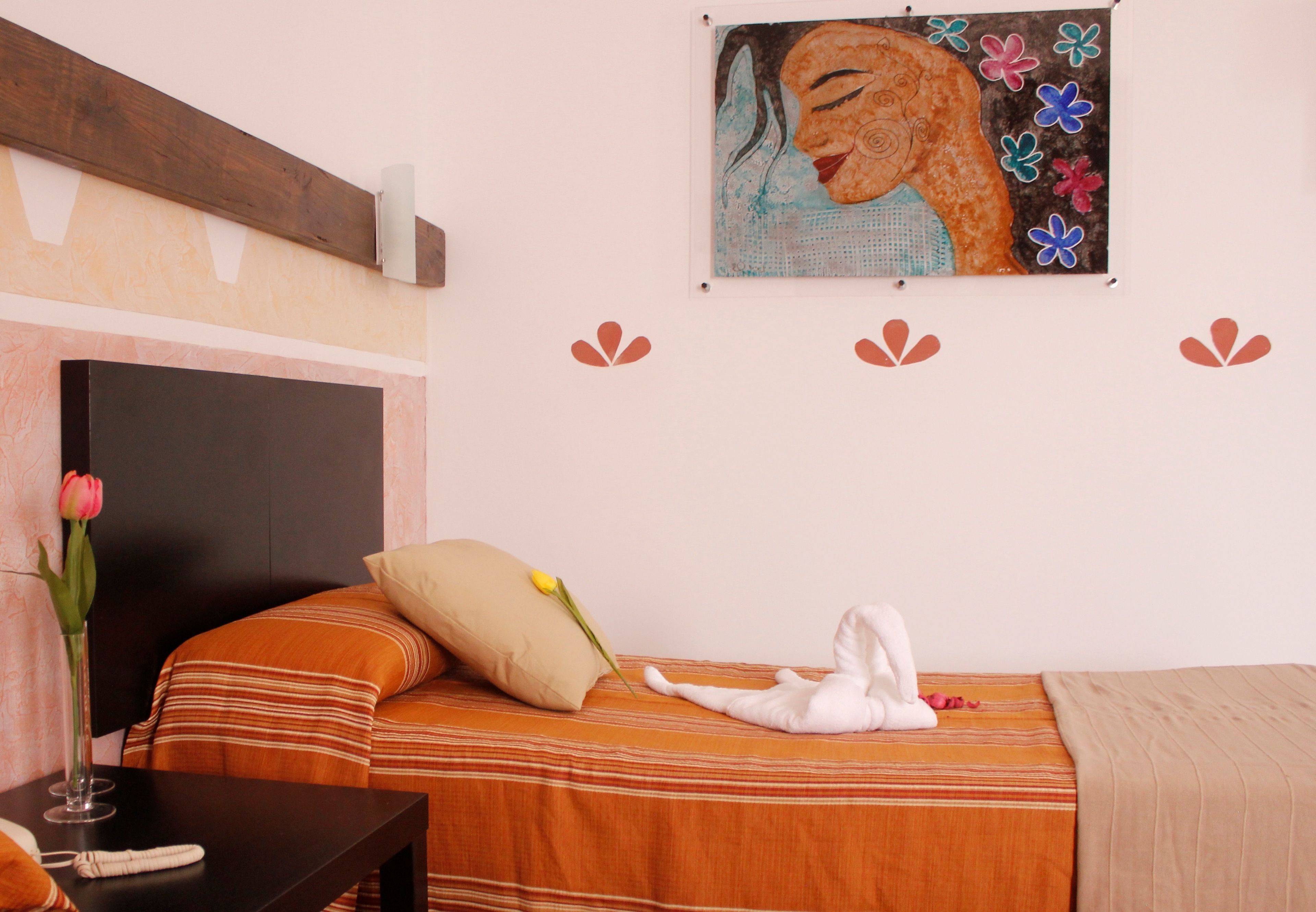 A hotel room with a bed, a bedside table with a vase of flowers, a painting on the wall, and a wooden headboard.