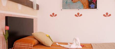 A hotel room with a bed, a bedside table with a vase of flowers, a painting on the wall, and a wooden headboard.