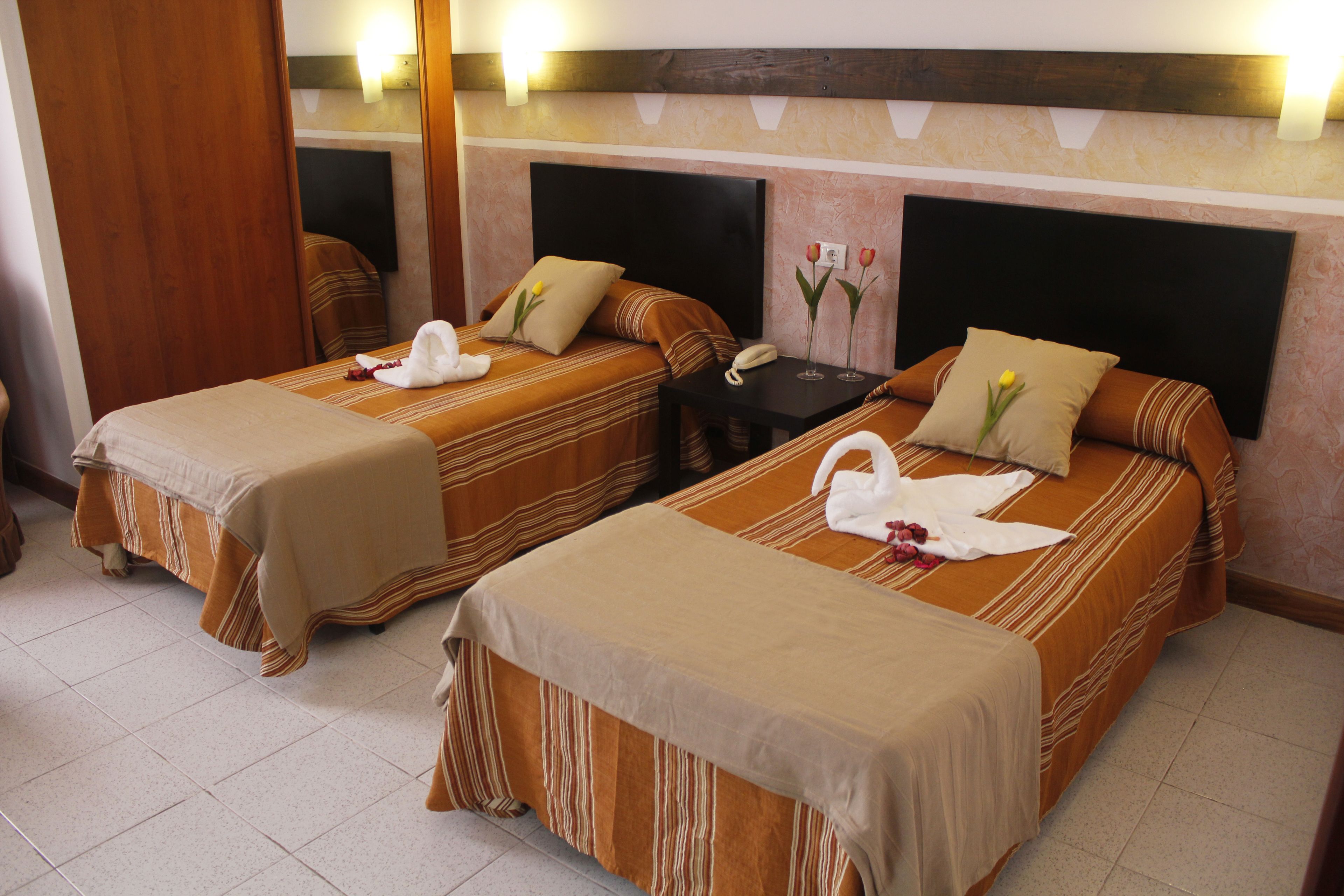 Two single beds with striped bedding, a bedside table with a phone, and a wall-mounted TV.