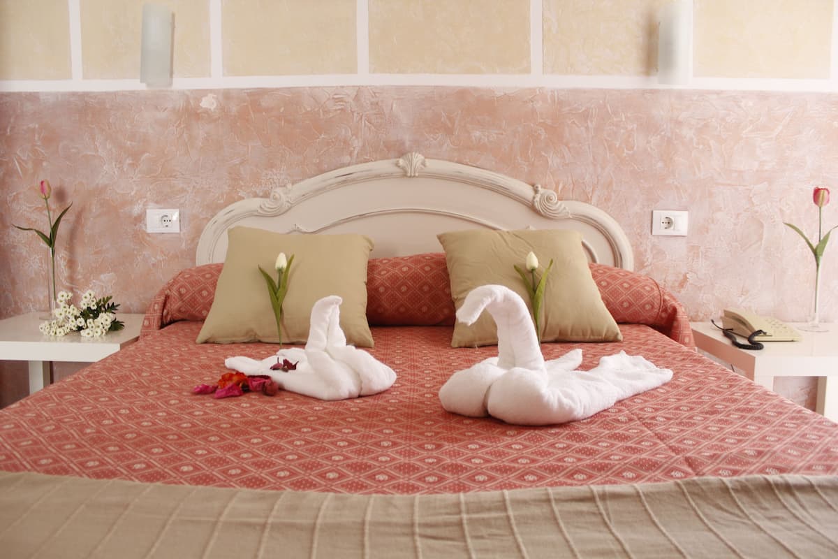 Un lit bien fait, recouvert d’une couvre-lit à motifs rouges, avec deux oreillers en forme de cygne et des serviettes également en forme de cygne.