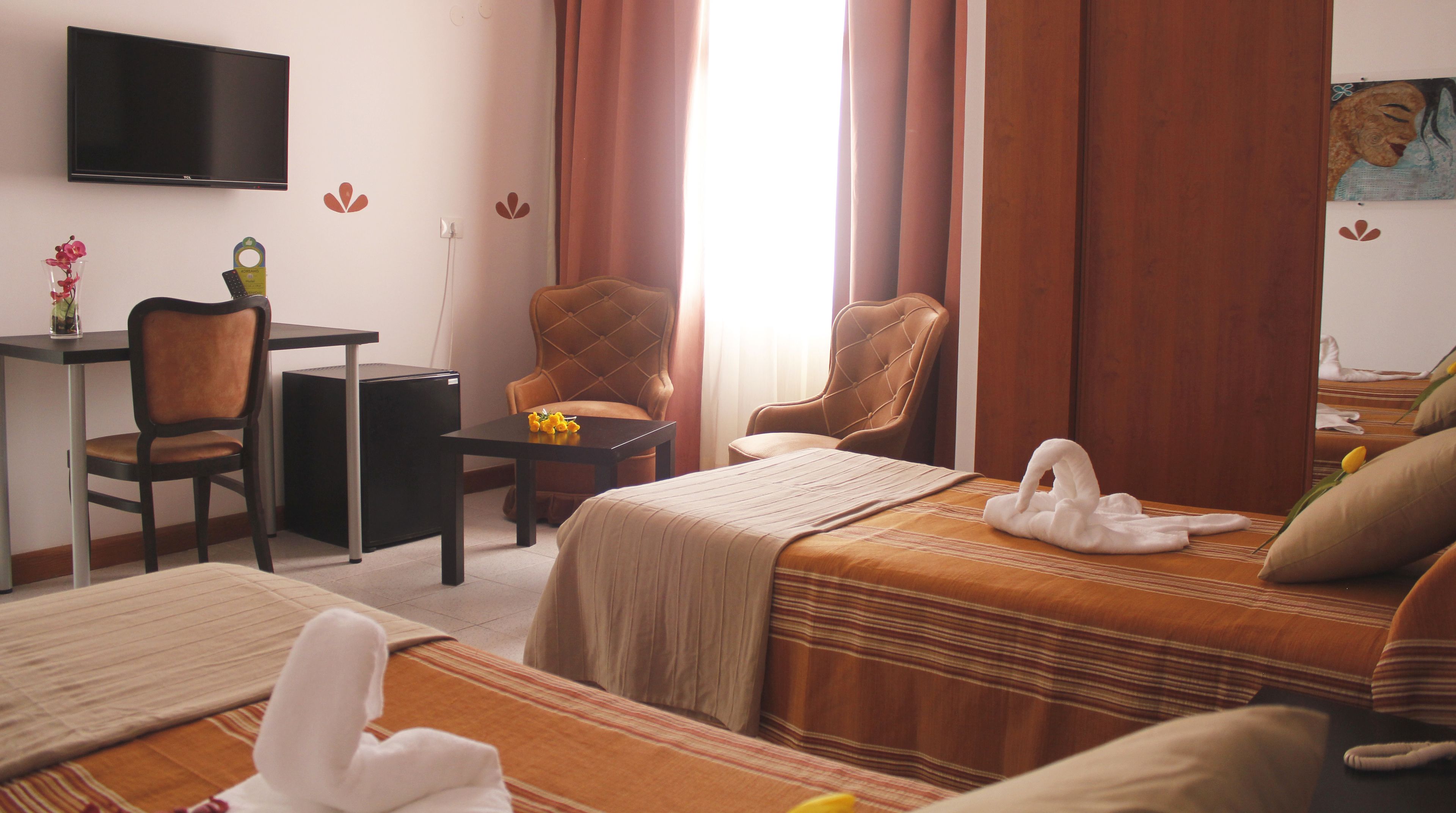 A hotel room with two beds, a desk, a chair, a TV, and a painting on the wall.