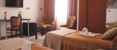 A hotel room with two beds, a desk, a chair, a TV, and a painting on the wall.