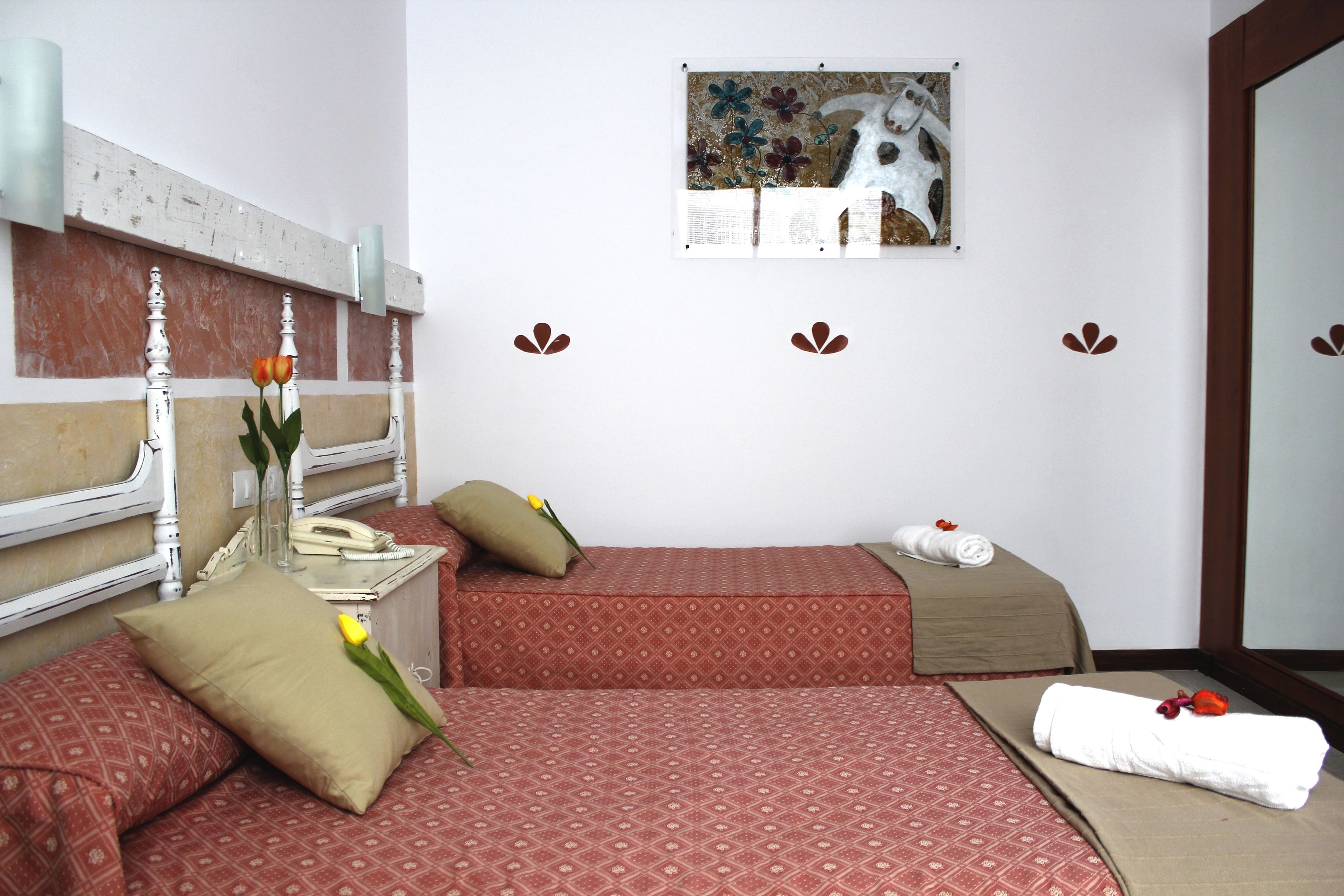 Une chambre d’hôtel avec deux lits, une table de chevet avec un téléphone, un vase de fleurs et un tableau au mur.