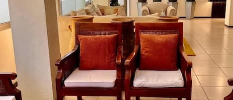 A lobby with two wooden chairs with red cushions, a small wooden table with a Christmas tree and white feathers, and a reception desk in the background.