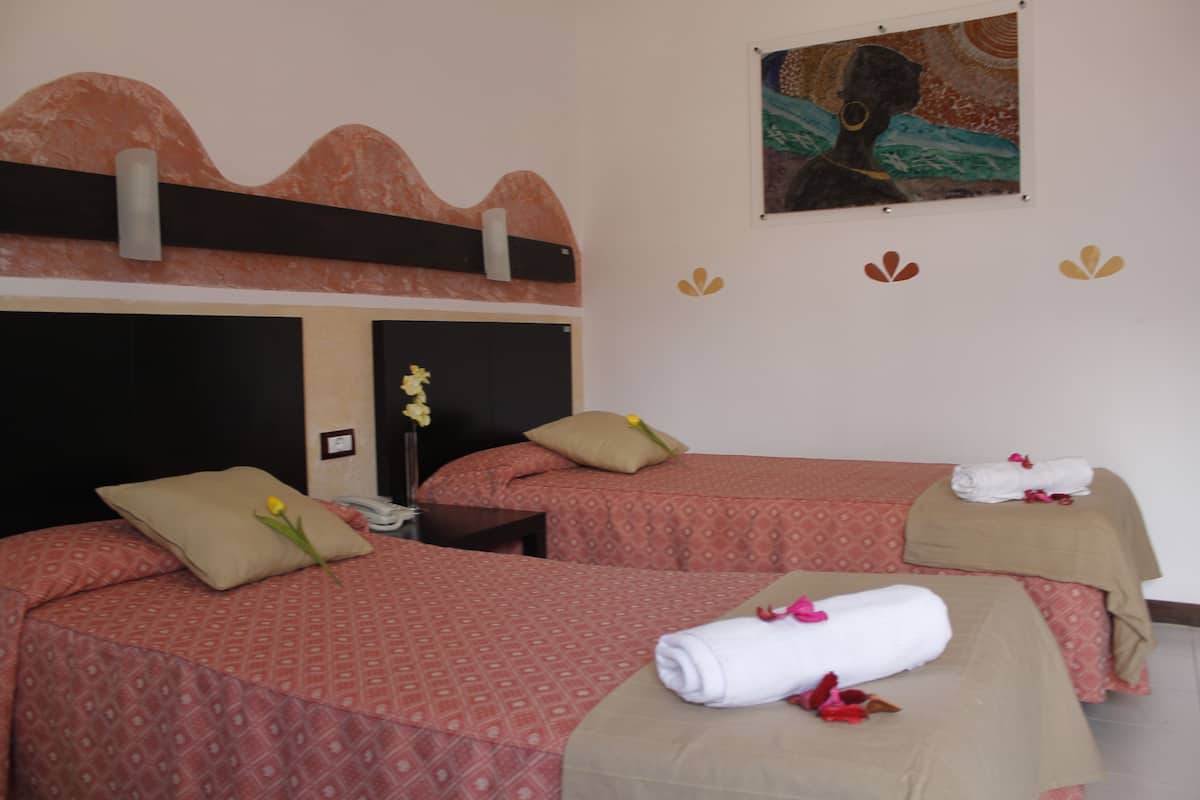 Une chambre d’hôtel avec deux lits, chacun recouvert d’une couvre-lit à motifs, une table de chevet, un téléphone et un tableau au mur.