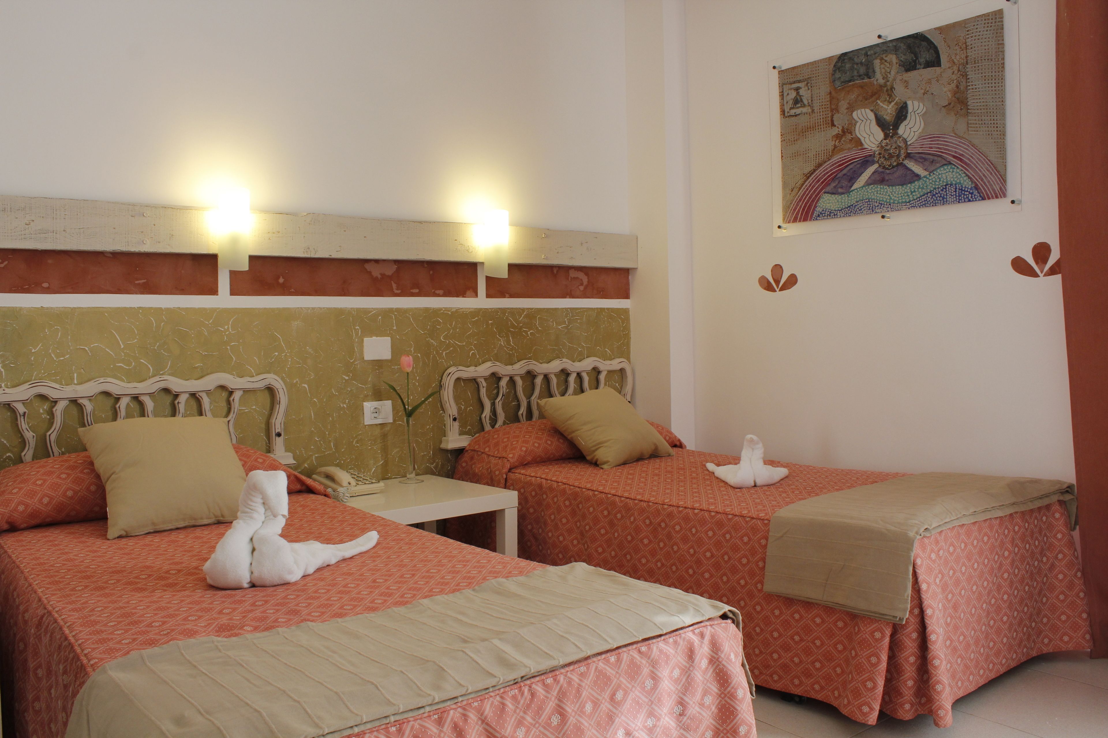 A hotel room with two beds, each with a patterned bedspread and pillows, a bedside table with a lamp, and a wall-mounted artwork.