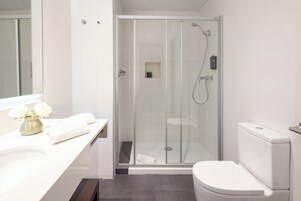 Ett modernt badrum med en duschavdelning med glasväggar, en vit toalett och en tvättställsmöbel med spegel och en vas med blommor.