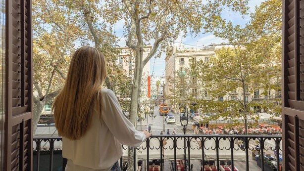 A balcony with a view of a city street, trees, and outdoor seating. - Arc la Rambla (Barcelona)