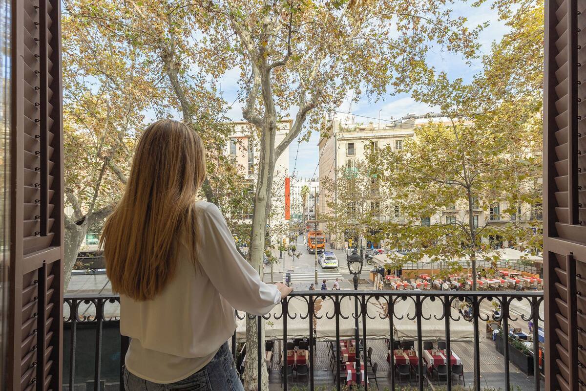 Un balcón con vista a una calle de la ciudad, árboles y mobiliario exterior.
