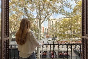 Un balcón con vista a una calle de la ciudad, árboles y mobiliario exterior.