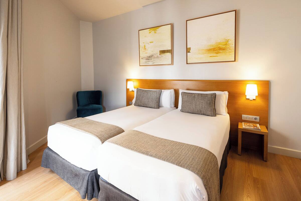 Una habitación de hotel con dos camas, una silla y una obra de arte en la pared.