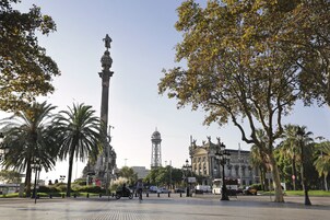 Una plaza con un monumento alto, palmeras y una torre a lo lejos.