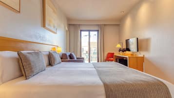 Ein Hotelzimmer mit einem großen Bett, einem Schreibtisch mit Fernseher, einem Sessel und einem Balkon mit Tisch und Stühlen.