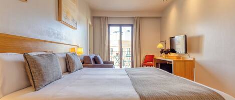 A hotel room with a large bed, a desk with a TV, a chair, and a balcony with a table and chairs.