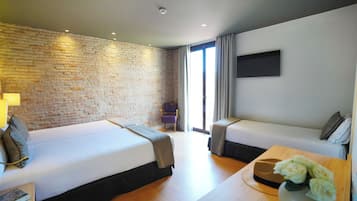 Una habitación de hotel moderna con dos camas, una pared de ladrillo, un televisor de pantalla plana y una mesa de centro de madera con un jarrón de flores.