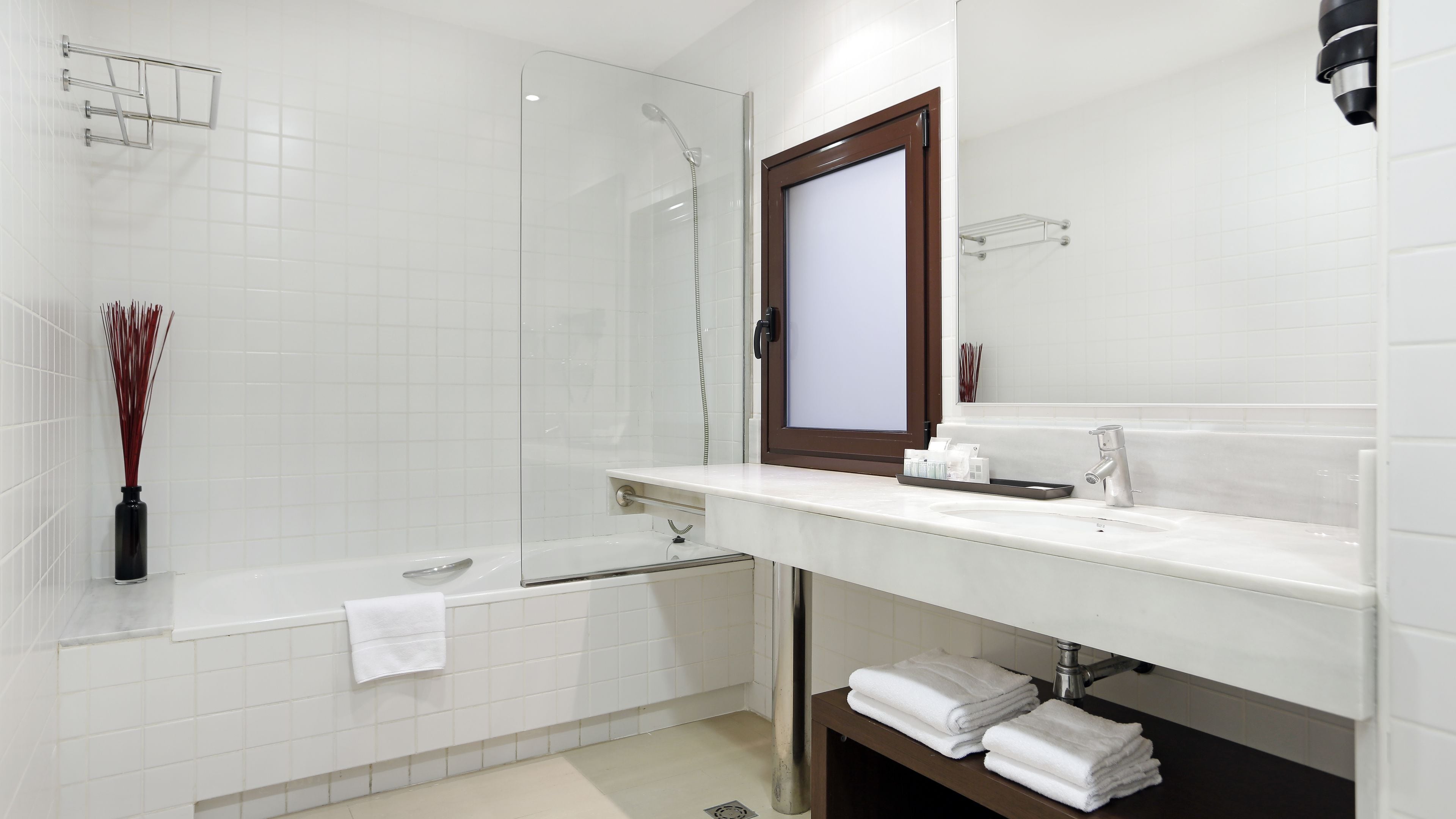 Uma casa de banho moderna com cabine de duche em vidro, lavatório branco com espelho e porta-toalhas.