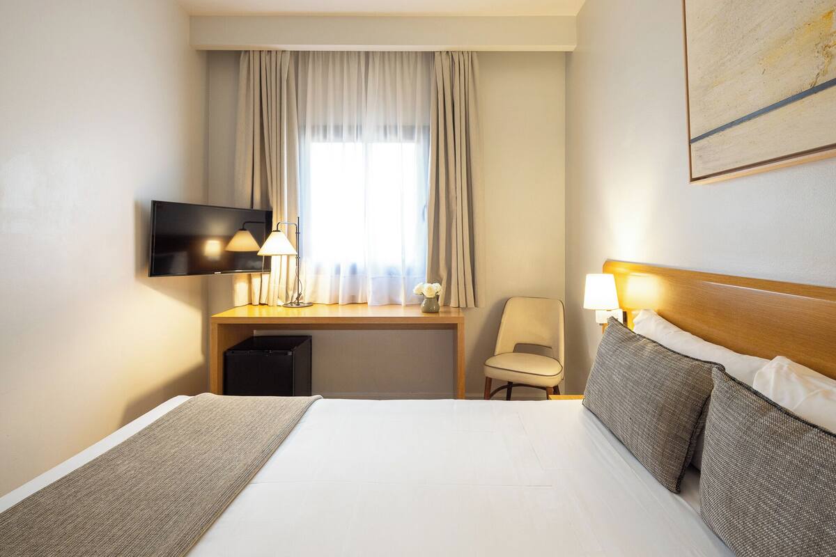 Habitación de hotel con cama, escritorio, silla, televisor y un cuadro en la pared.
