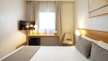 A hotel room with a bed, a desk, a chair, a TV, and a painting on the wall.
