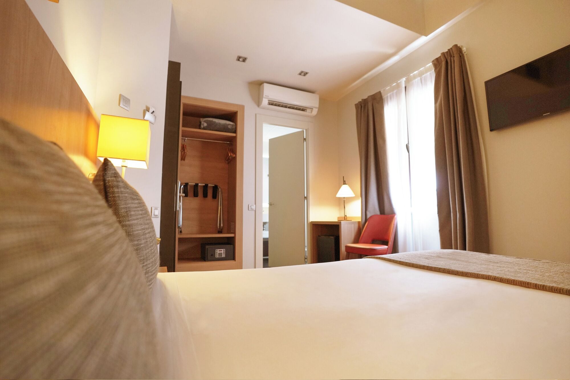 A hotel room with a bed, a wardrobe, a desk, a chair, and a TV.