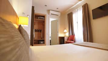A hotel room with a bed, a wardrobe, a desk, a chair, and a TV.