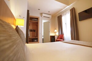 A hotel room with a bed, a wardrobe, a desk, a chair, and a TV.