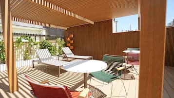 Un patio exterior techado con listones de madera, una mesa redonda y varios sillones de descanso.