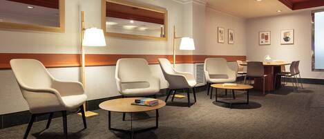 A hotel lobby with seating areas, a reception desk, and framed artwork on the walls.