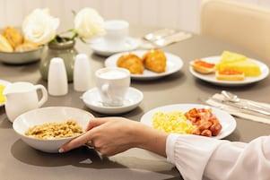 A breakfast setting with various dishes, including eggs, bacon, and pastries, on a table with cups and a vase of flowers.