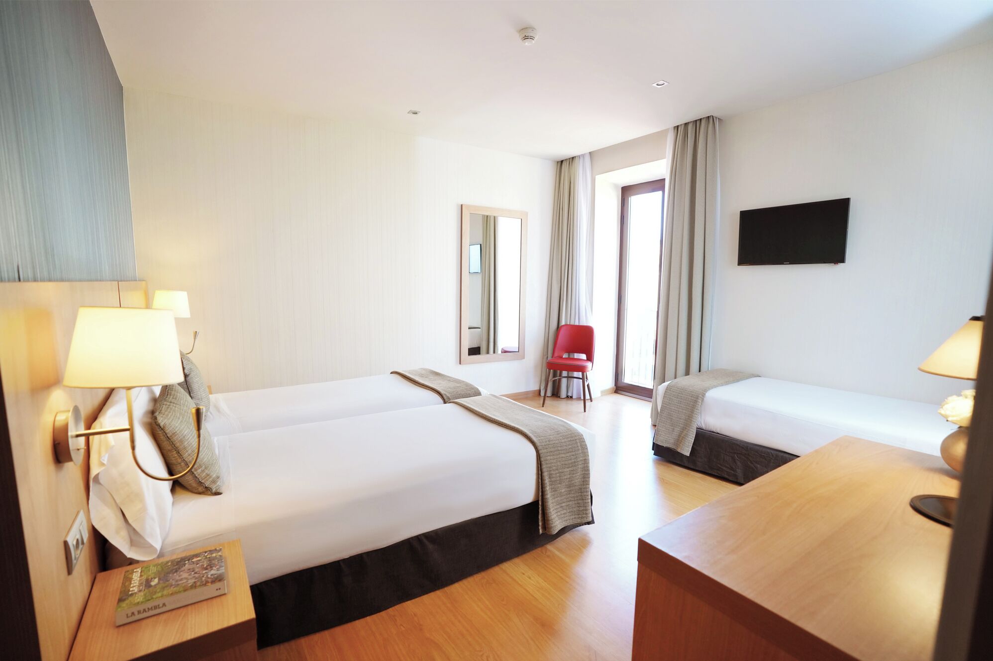 A hotel room with two beds, a desk, a chair, a TV, and a window with curtains.