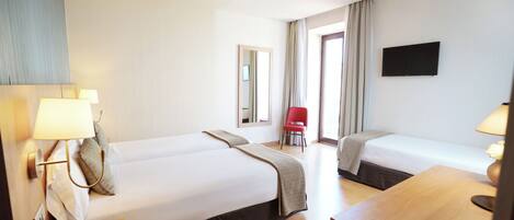 A hotel room with two beds, a desk, a chair, a TV, and a window with curtains.