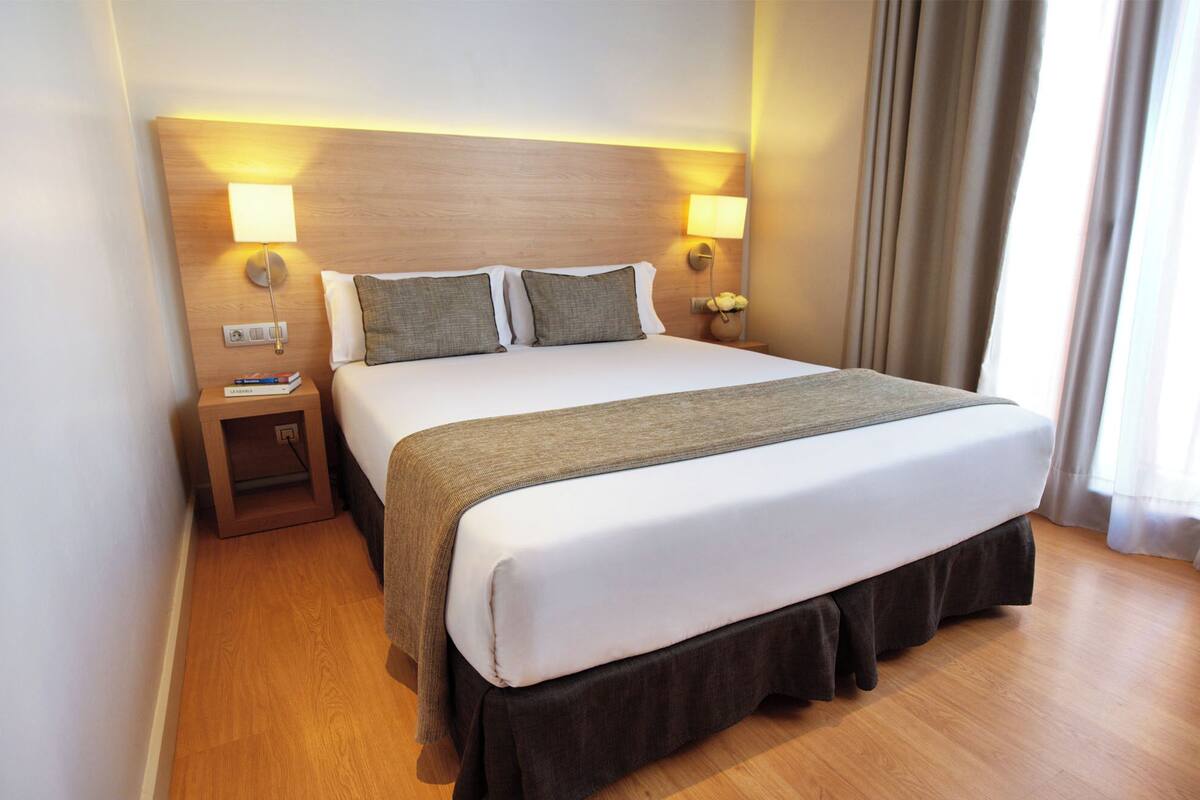 Habitación de hotel con una cama grande, dos lámparas de noche, una mesita de noche y un cabecero de madera.