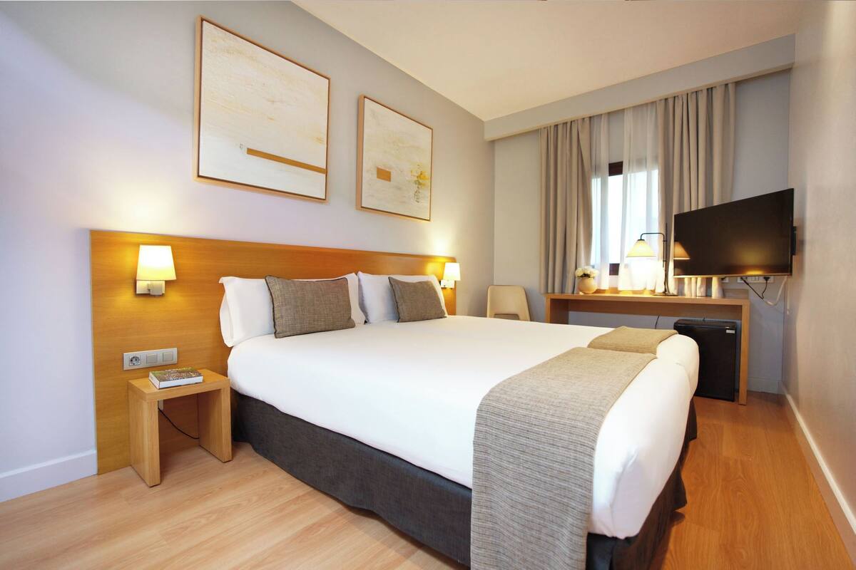 Habitación de hotel con una cama grande, lámparas de noche, un escritorio con televisión de pantalla plana y un refrigerador pequeño.