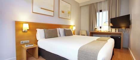 Habitación de hotel con una cama grande, lámparas de noche, un escritorio con televisión de pantalla plana y un refrigerador pequeño.