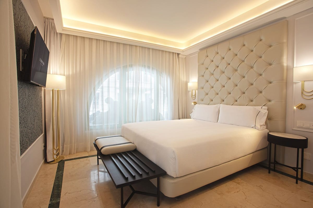 Une chambre d’hôtel moderne avec un grand lit, un banc, une télévision et une table de chevet.