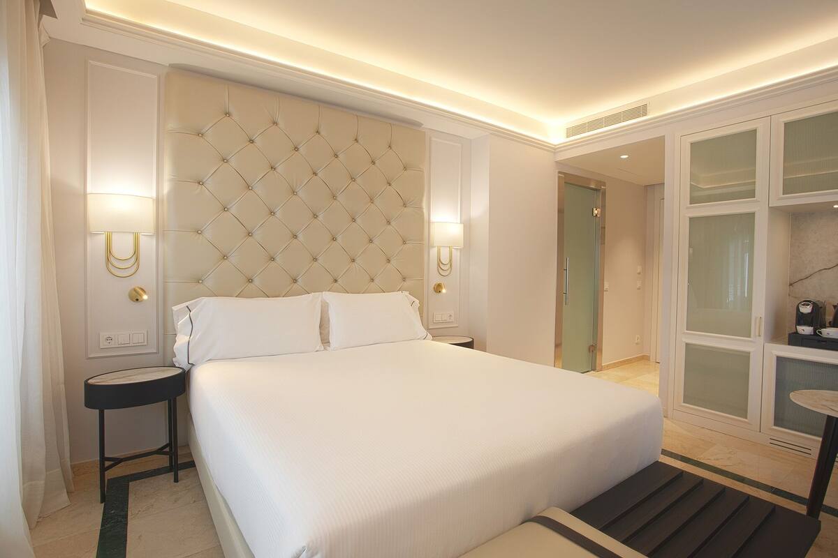 Une chambre d’hôtel bien aménagée, avec un grand lit, des tables de chevet, une armoire et une petite table sur laquelle se trouve une bouilloire.