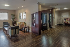 Un vestíbulo de hotel con mostrador de recepción, zona de estar y máquinas expendedoras.