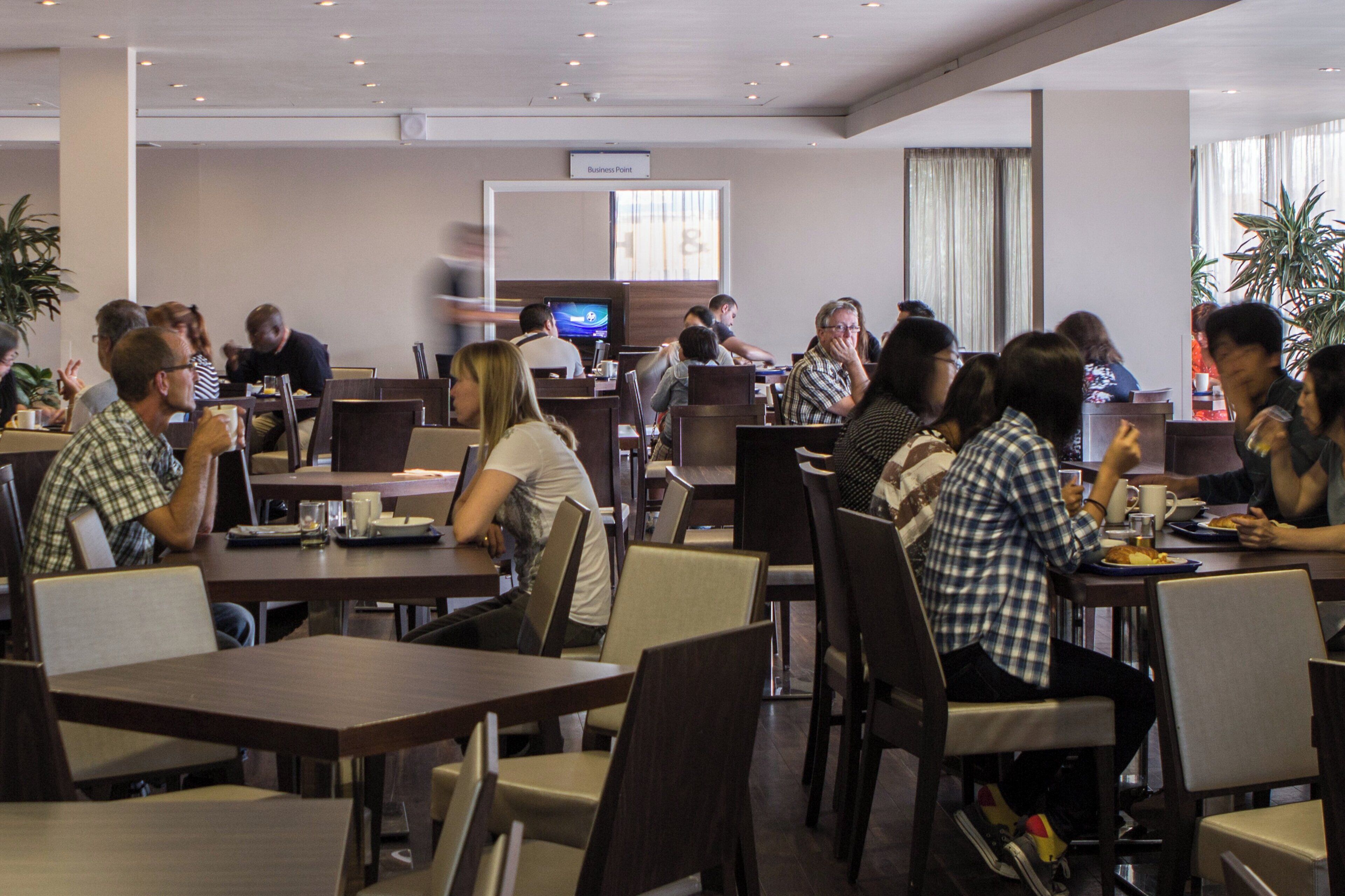 A dining area with multiple tables and chairs, some occupied by people.