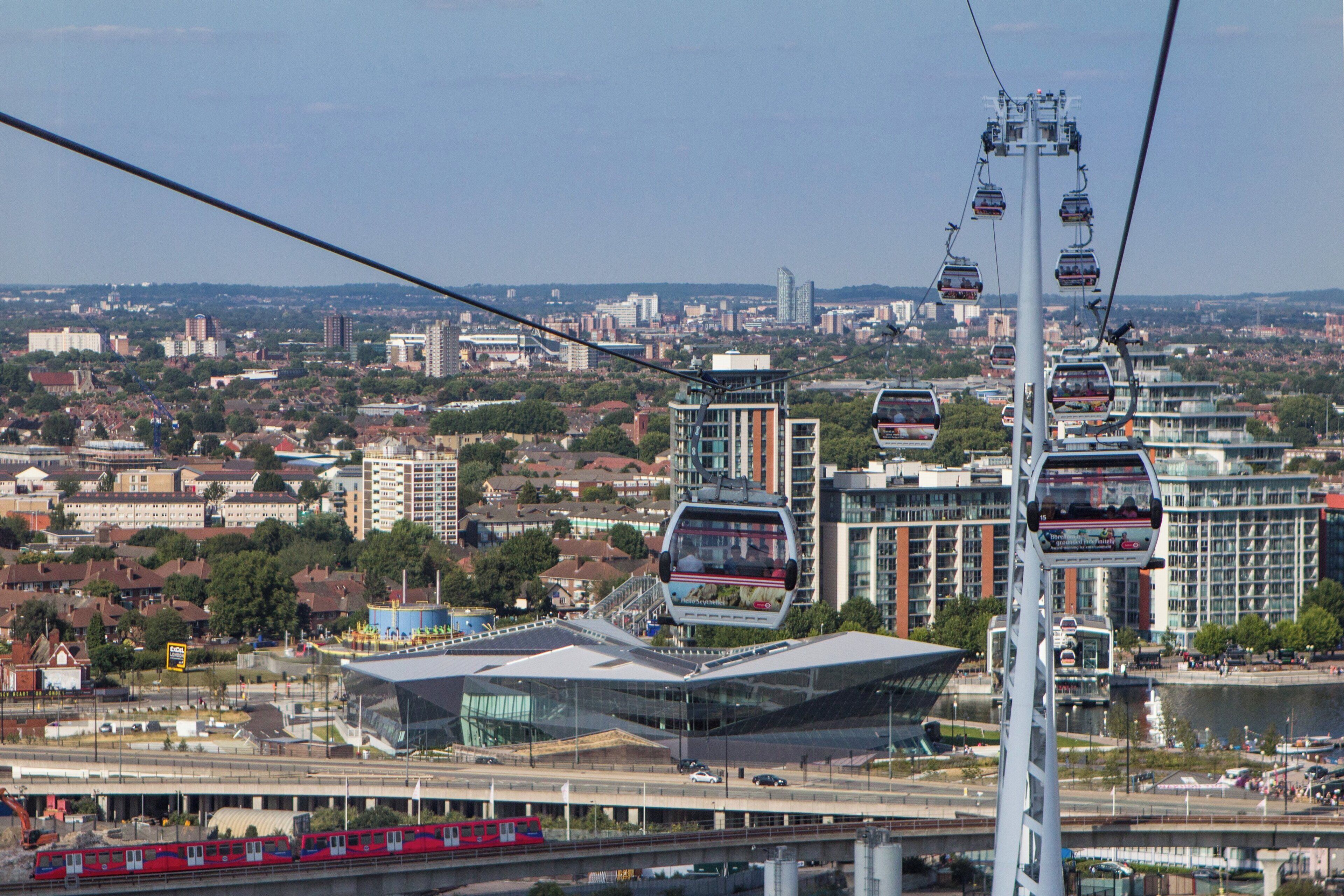A cable car system with multiple cabins, a modern building with a glass facade, and a train passing by.