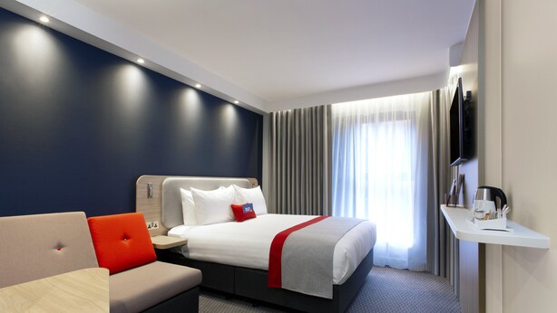 A modern hotel room with a bed, a sofa, a small table, and a TV mounted on the wall. - Holiday Inn Express London-Royal Docks, Docklands by IHG (London)