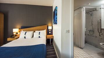 A hotel room with a bed, bedside lamps, a telephone, a painting, and a shower area.