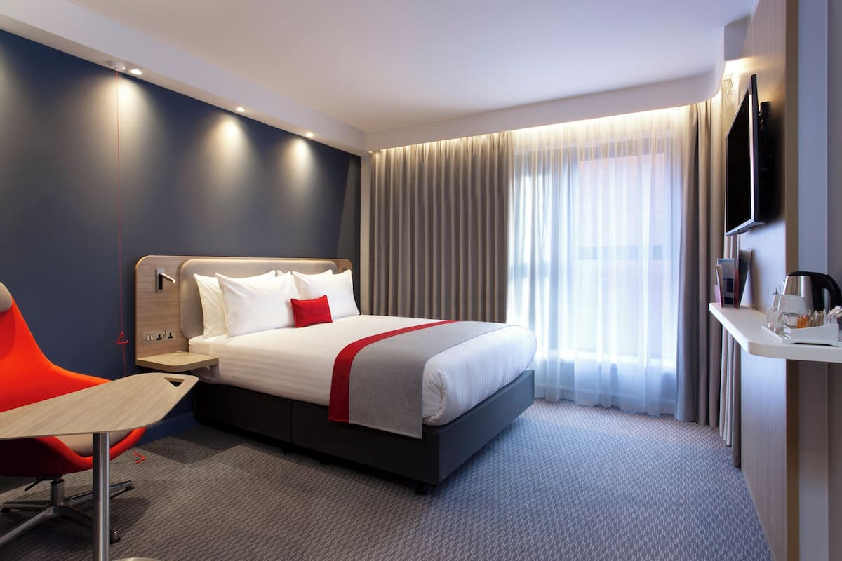 A modern hotel room with a large bed, a desk, a chair, and a TV.