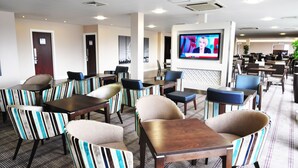 A hotel lobby with striped chairs, tables, a TV screen, and a patterned carpet. - Holiday Inn Express London-Royal Docks, Docklands by IHG (London)