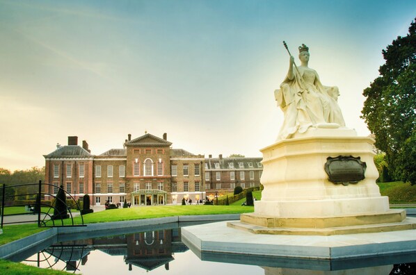 A classical statue on a pedestal in front of a large, historic building with a reflective pool.