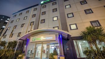 L’entrée d’un hôtel Holiday Inn Express, avec une porte en verre, une enseigne au-dessus de l’entrée et une rangée de palmiers devant.