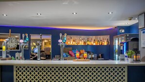 A bar area with multiple beer taps, a clock, and a variety of bottles. - Holiday Inn Express London-Royal Docks, Docklands by IHG (London)