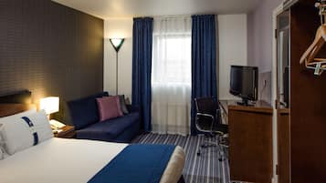 A hotel room with a large bed, a sofa, a desk with a television, and a wardrobe.