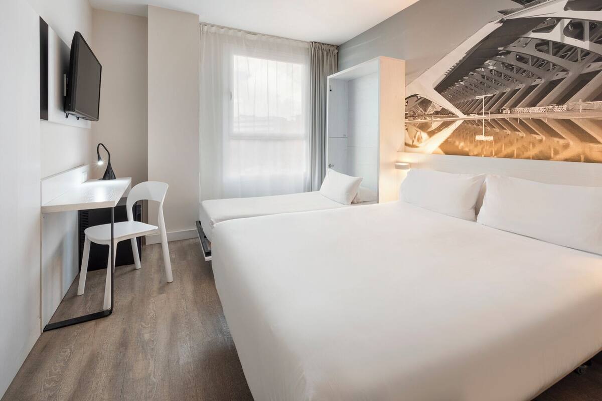 Une chambre d’hôtel avec un grand lit, un bureau avec une chaise, une télévision et une vue sur un pont.