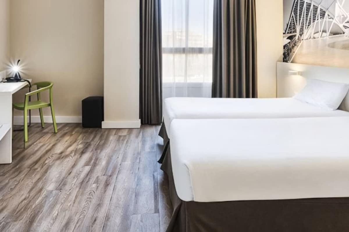A hotel room with a bed, a desk, a chair, and a window with curtains.