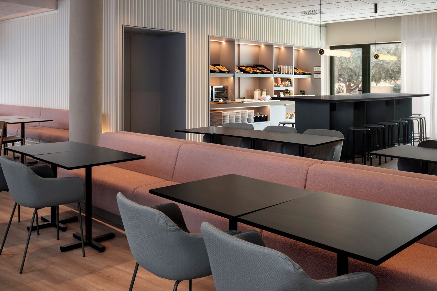 Un café moderno con una barra larga, zona de estar y vistas al exterior.