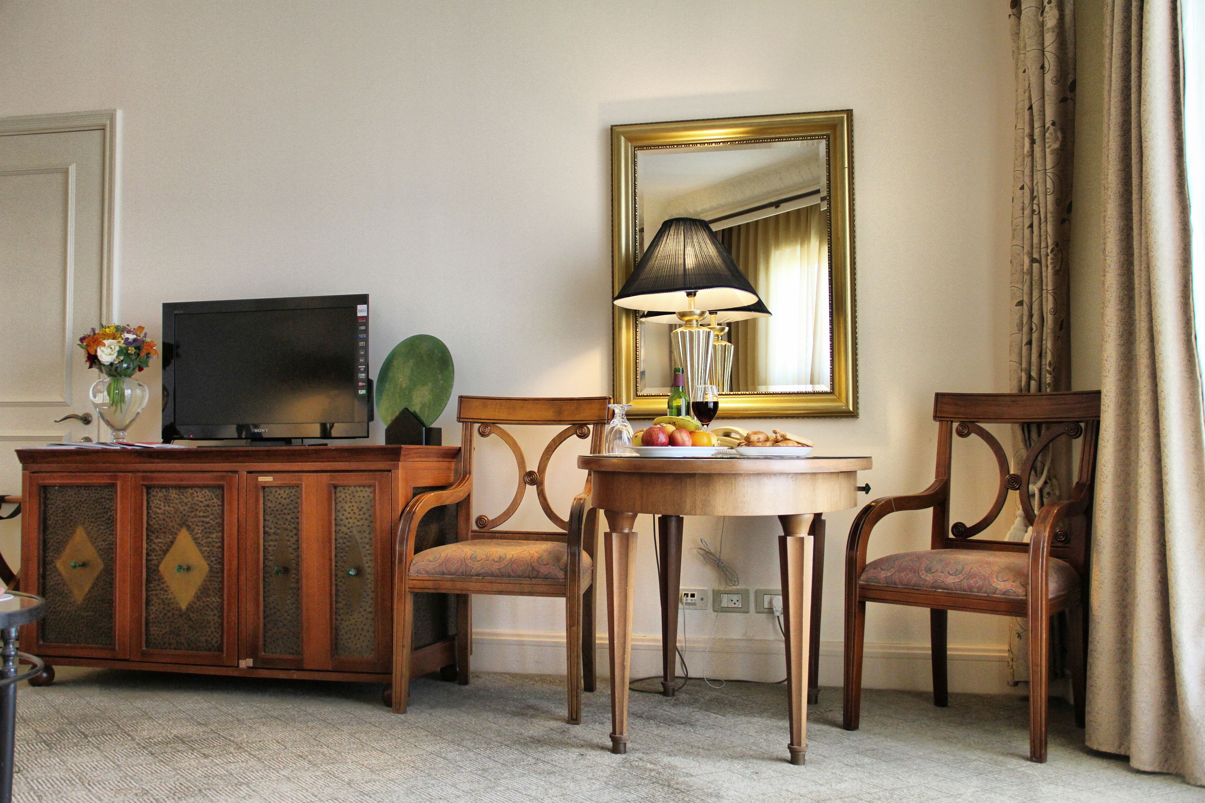 A hotel room with a wooden cabinet, a television, a table with fruit, a lamp, and a mirror.